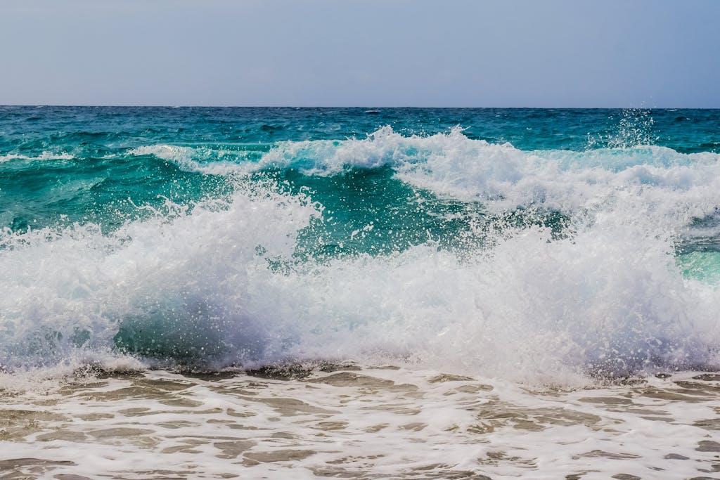 Dynamic ocean waves crashing onto a sandy shore under daylight, showcasing nature's power and beauty. Photo by Pixabay